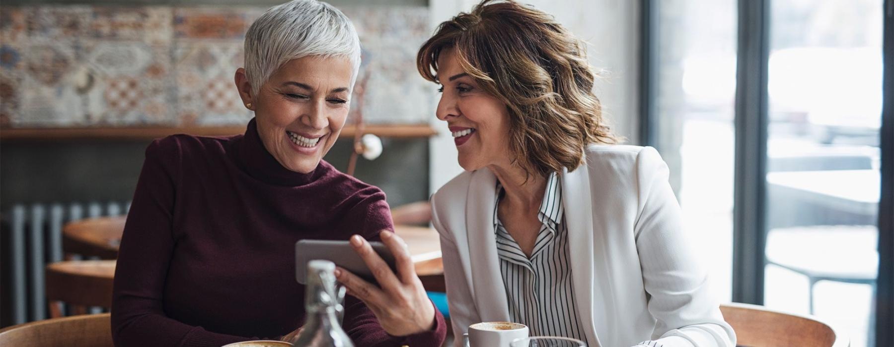 two women sitting at a table looking at a phone