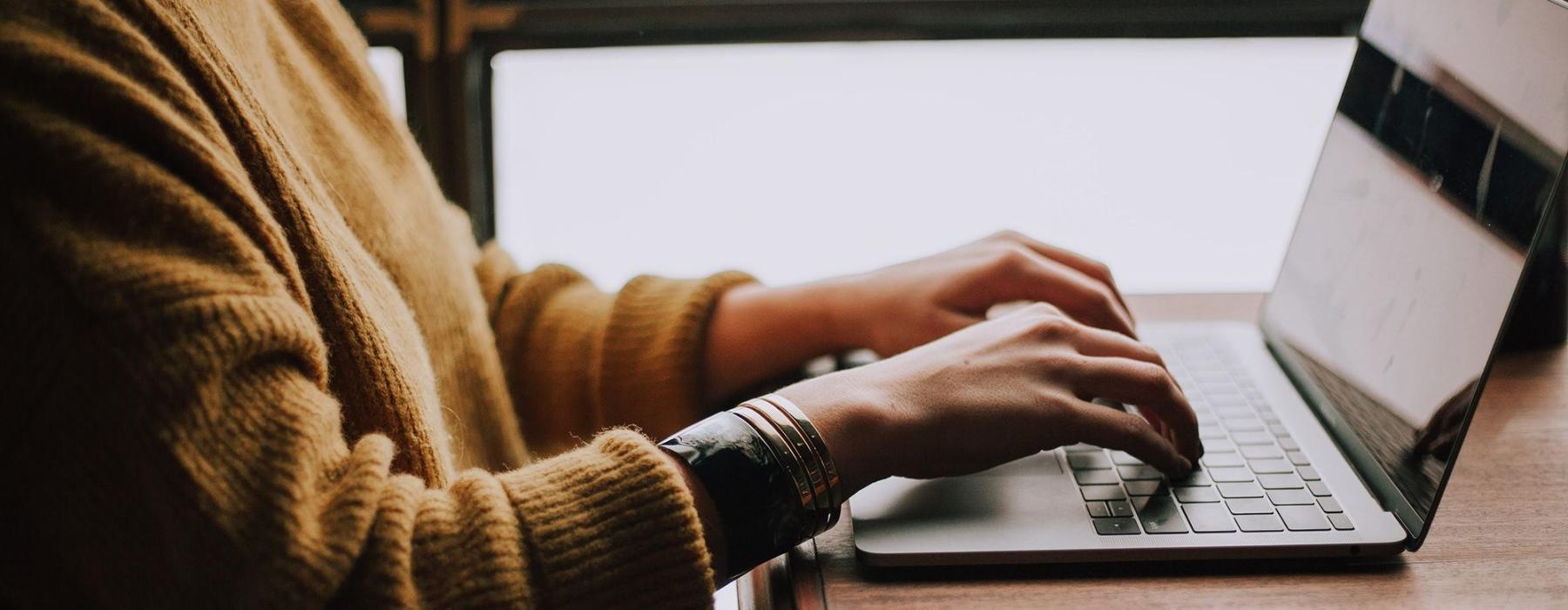 woman types on her laptop near large window